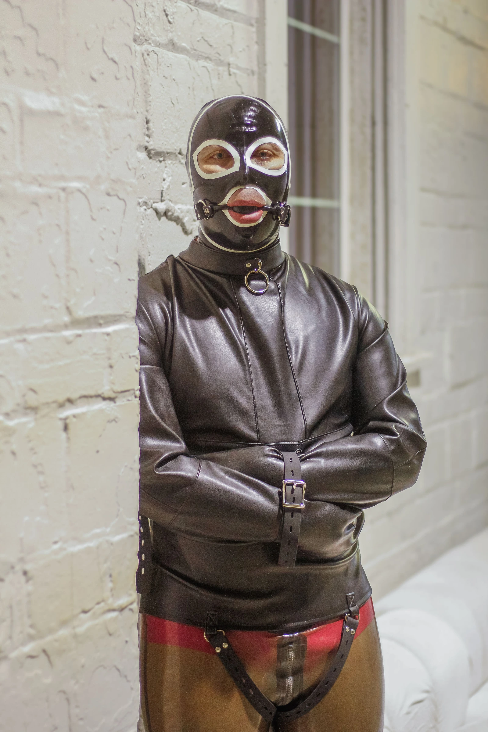 Full-body front portrait of a wearer in the Asylum Adventurer black synthetic leather straitjacket.
