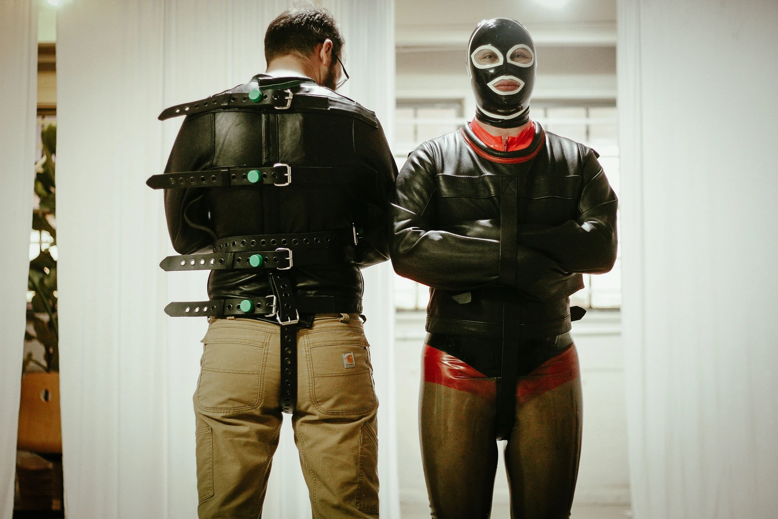 Two Leather Posey Replica wearers showing front crossed sleeves and rear buckle closures.